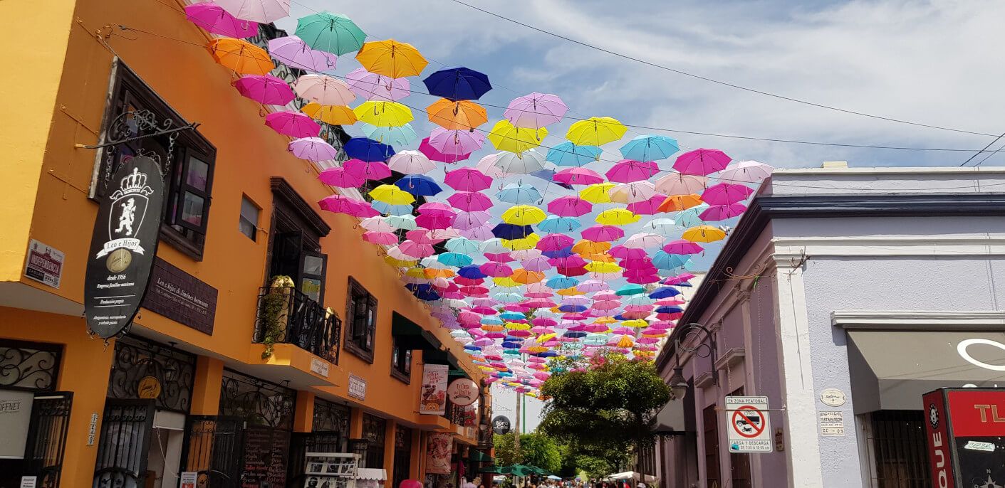 Bunte Regenschirme hängen über einer Straße, gesäumt von Gebäuden in lebhaften Farben. Einladende Atmosphäre.
