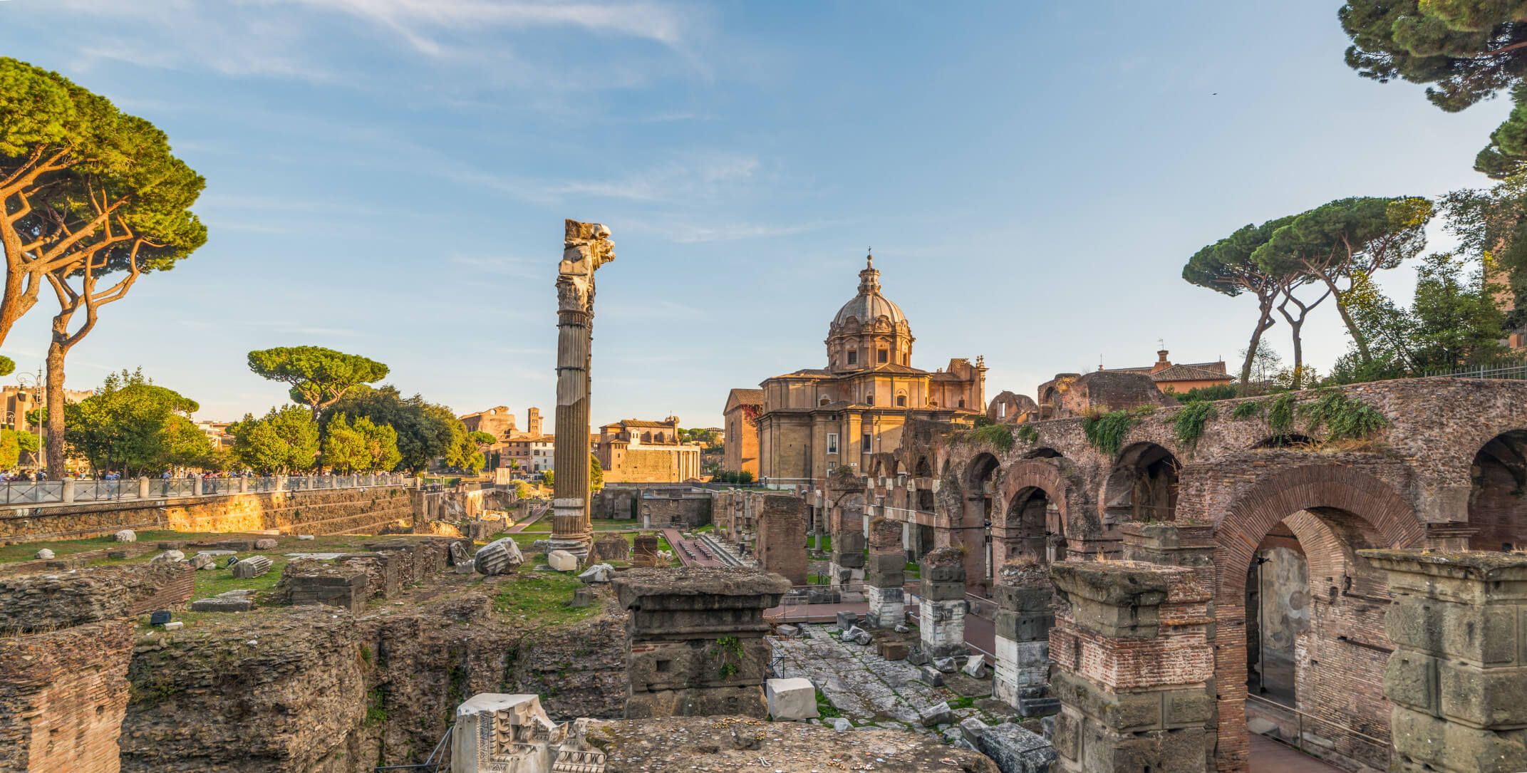 Die Ruinen des antiken Roms mit historischen Gebäuden und Bäumen unter klarem Himmel.