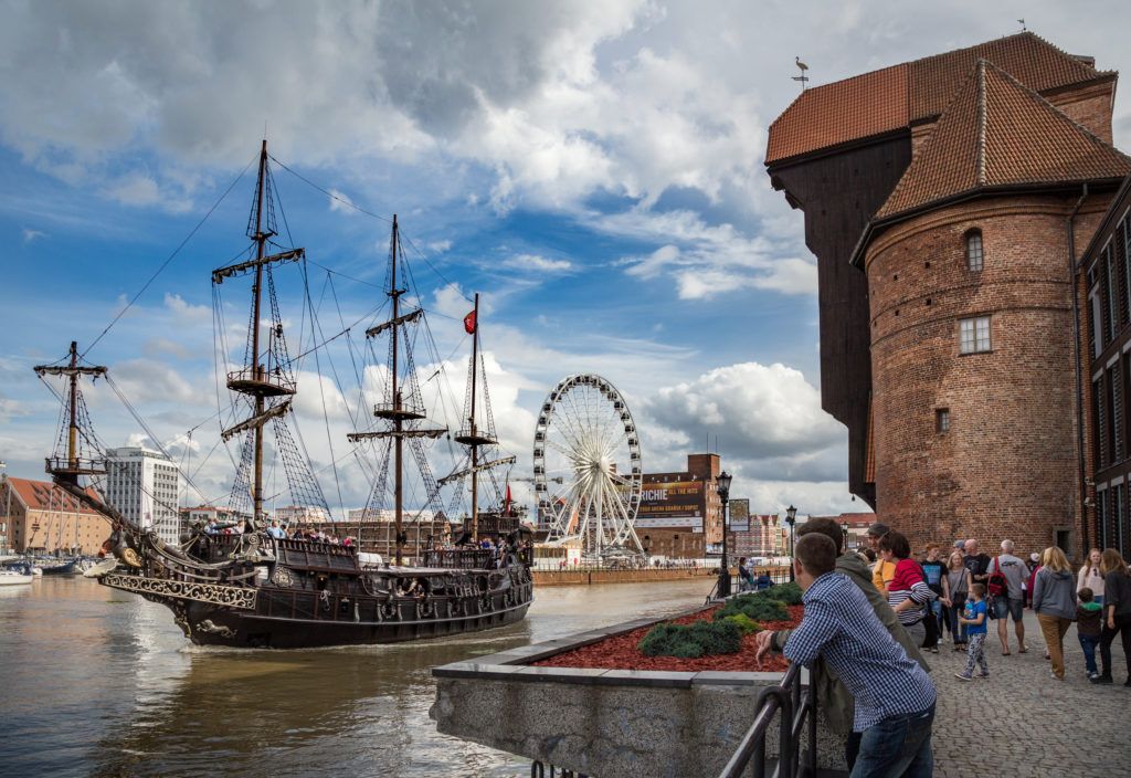Ein historisches Schiff fährt am Wasser entlang, während Menschen die Aussicht und das Riesenrad genießen.
