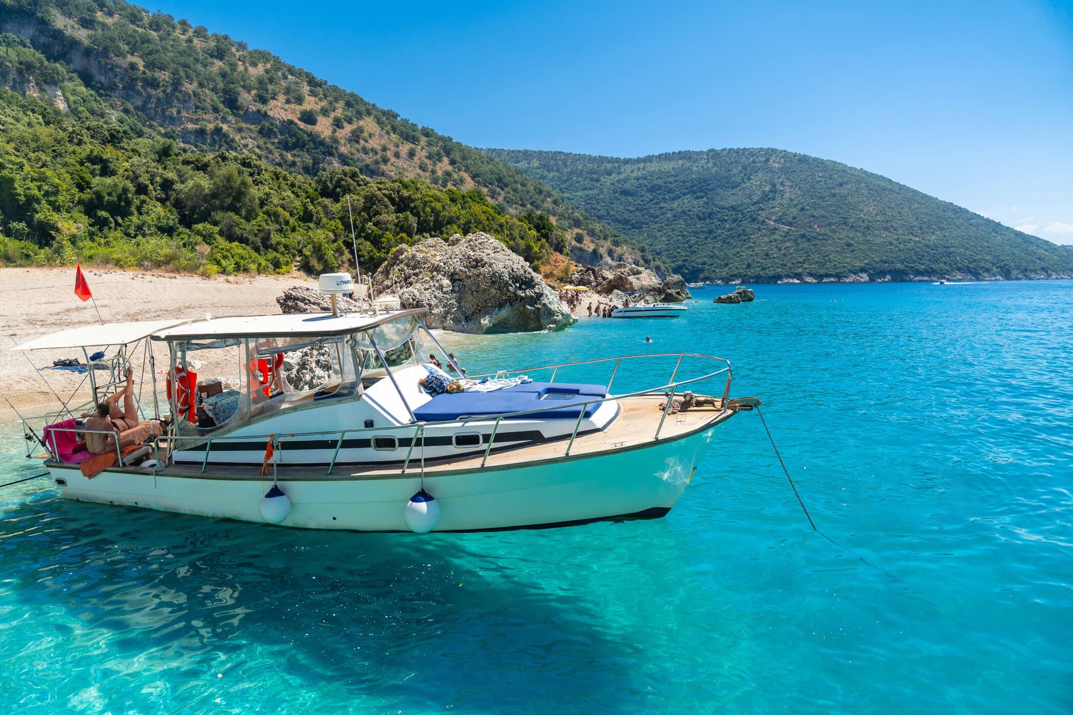 Ein Boot liegt im klaren blauen Wasser, umgeben von grünen Hügeln und einem schönen Strand. Sonne und Entspannung pur!