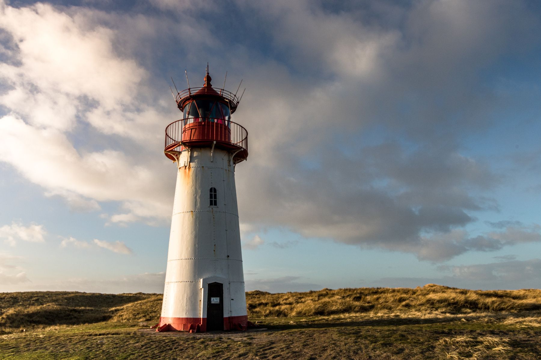 Der Leuchtturm steht markant in der Landschaft, umgeben von sanften Hügeln und einem dramatischen Himmel.