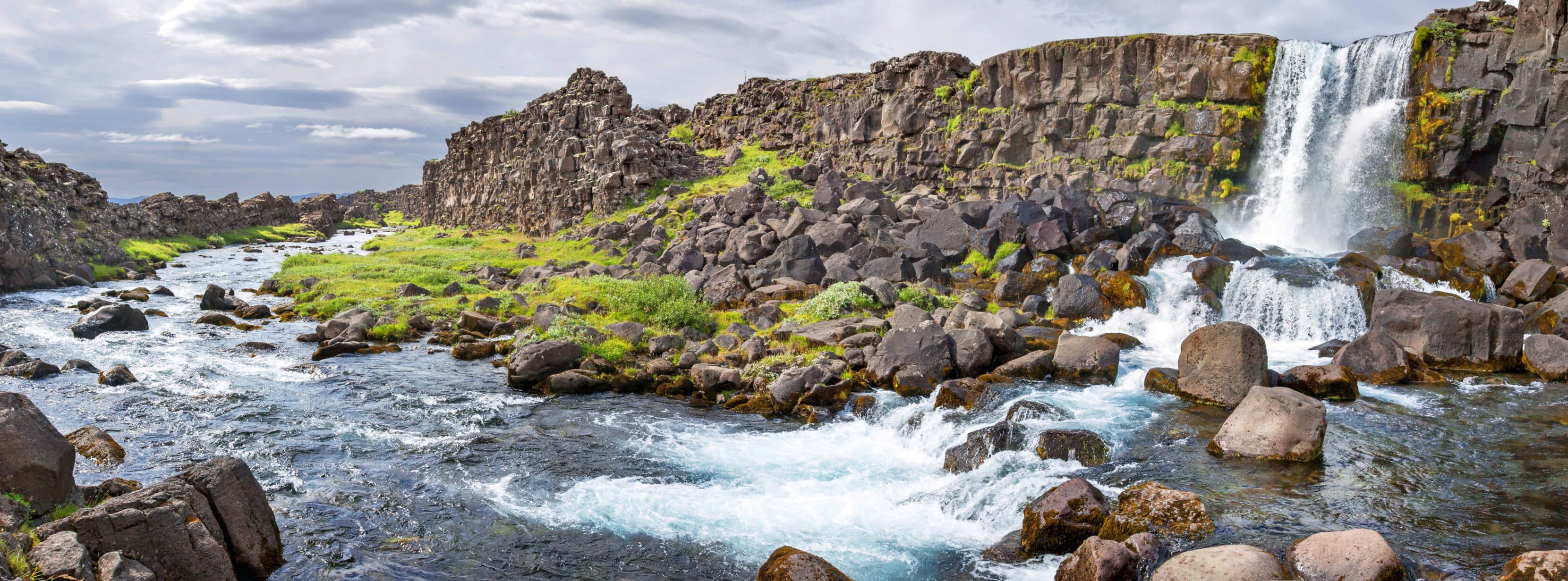 Ein beeindruckender Wasserfall im grünen Tal, umgeben von Felsen und einem klaren, fließenden Bach.