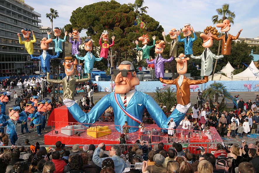 Großer Karnevalswagen mit bunten, überdimensionalen Figuren und fröhlichen Menschenmengen in Feierlaune.