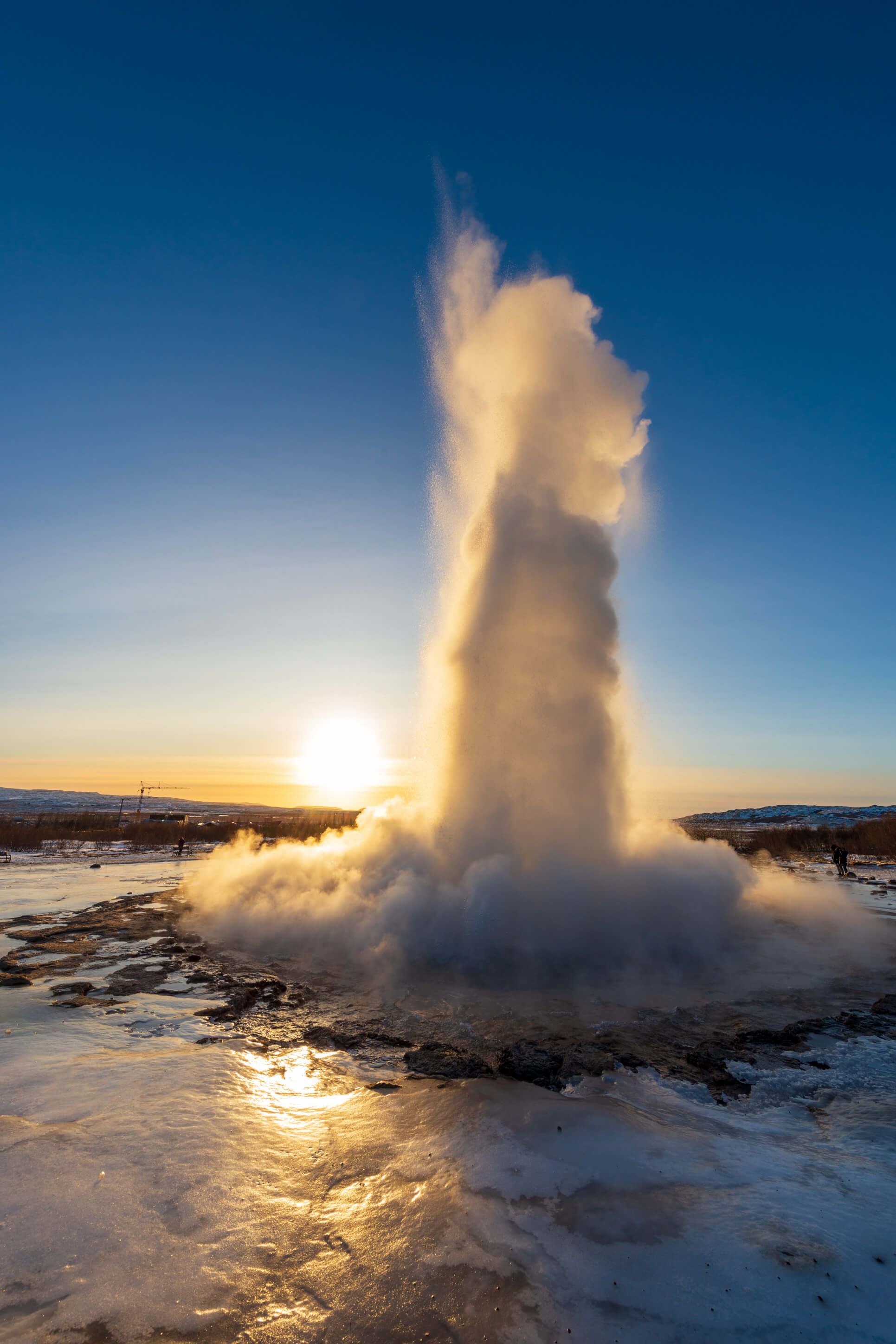 Ein Geysir sprudelt in den Sonnenuntergang, umhüllt von Dampf und frischem Licht, beeindruckende Naturgewalt.