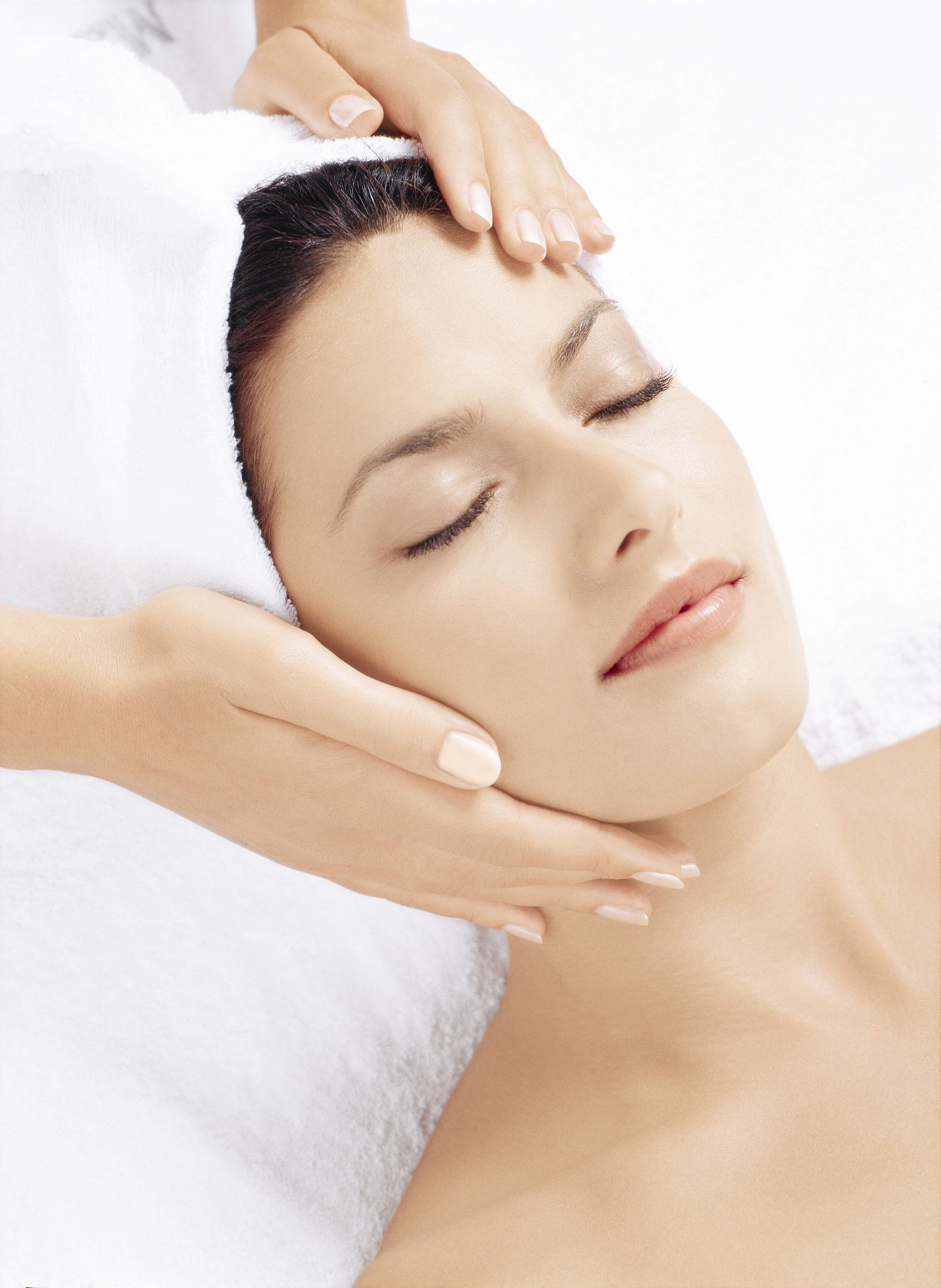 Eine Frau entspannt bei einer Gesichtsbehandlung, mit geschlossenen Augen und einer Hand auf ihrem Gesicht.