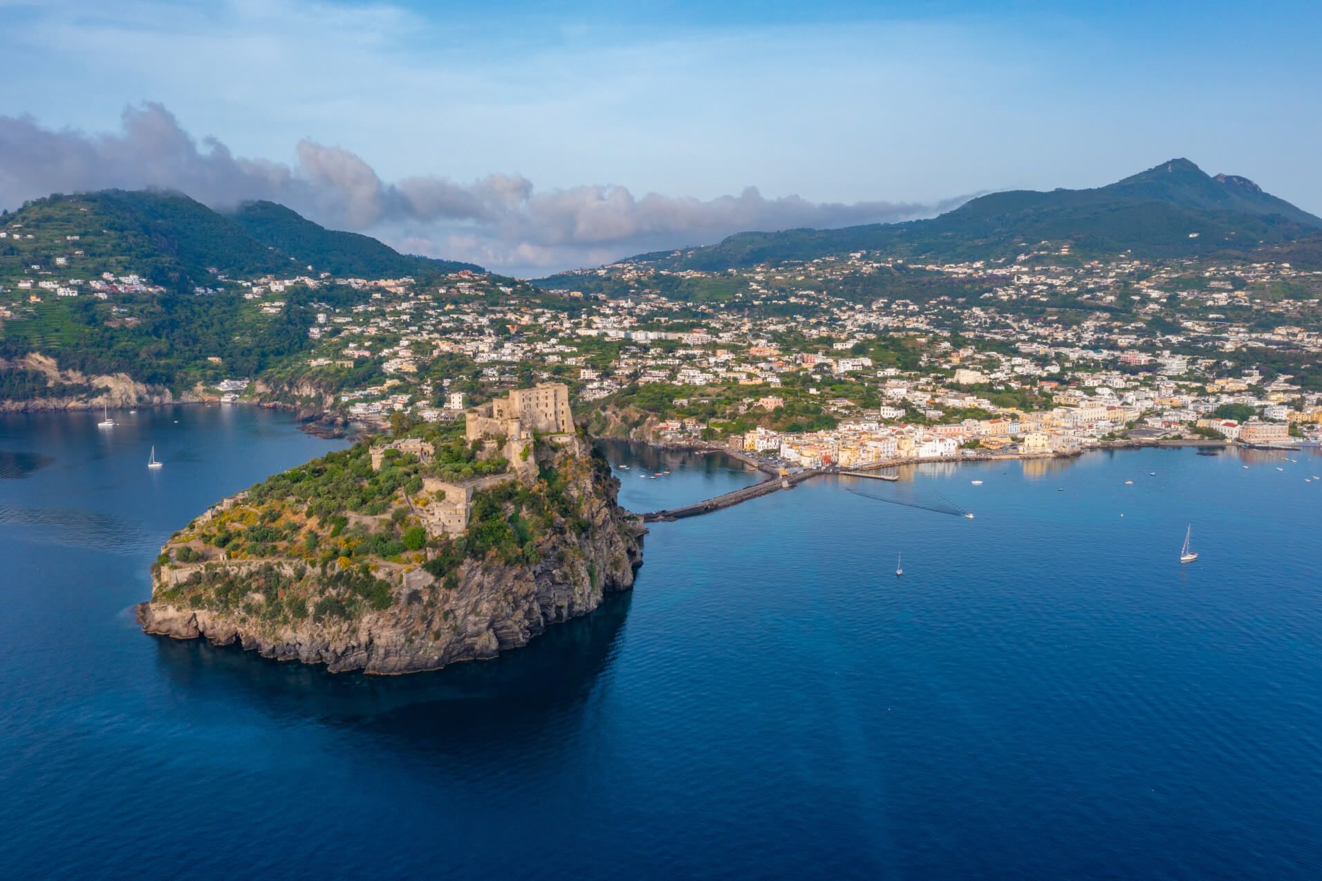 Eine Luftaufnahme einer malerischen Küstenlandschaft mit einer Festung auf einem Felsen und einer Stadt im Hintergrund.