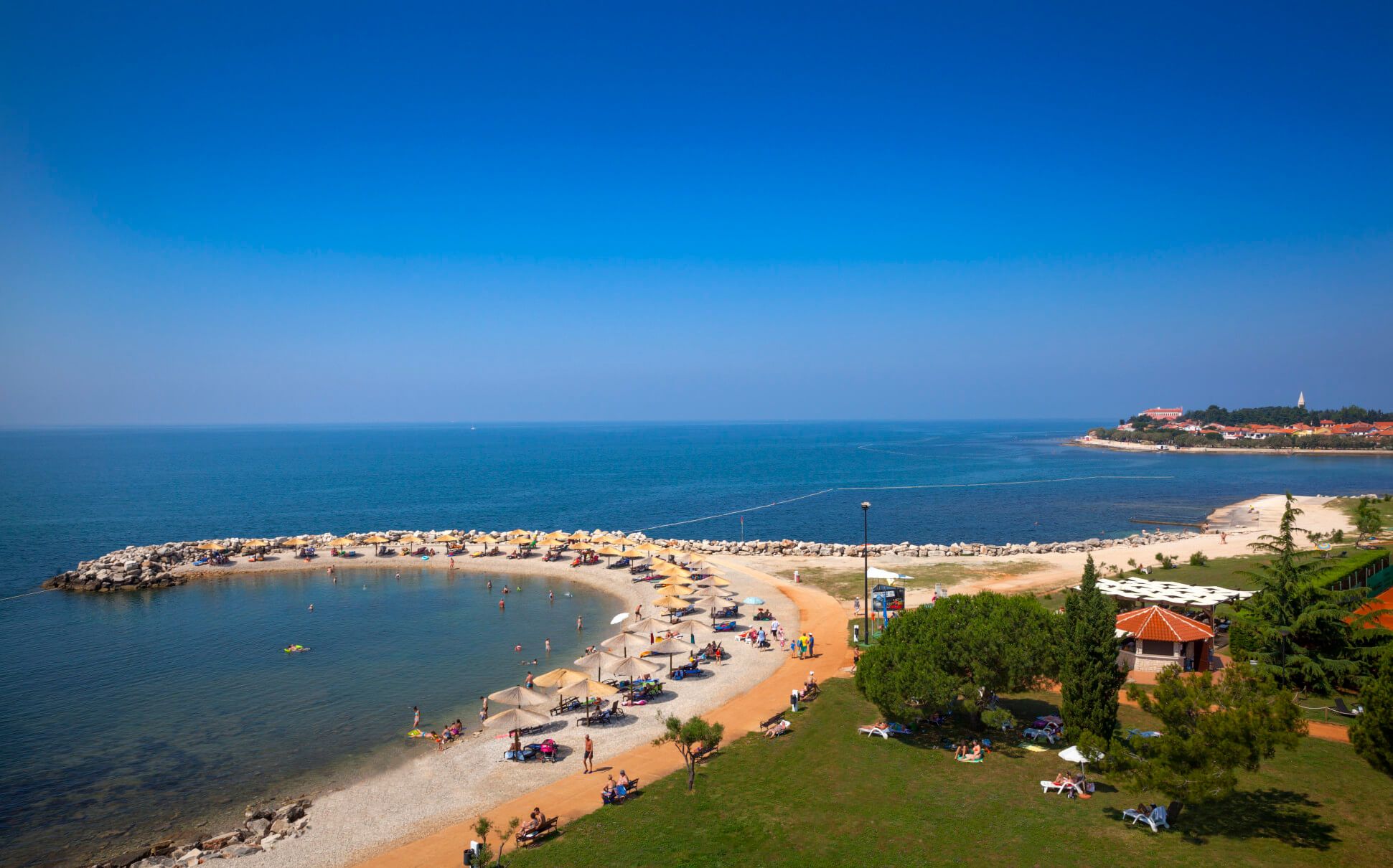 Ein malerischer Strand mit Sonnenschirmen, klarem Wasser und blauen Himmel an einer Küstenlinie.