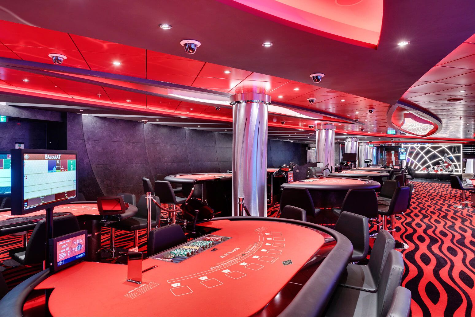 Elegantes Casino mit roten Tönen, Tischspielen und moderner Ausstattung in stilvollem Ambiente.