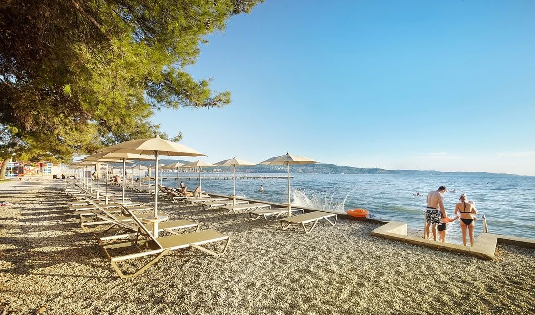 Ein schöner Strand mit Liegen, Sonnenschirmen und Lebensfreude am Wasser in sonnigem Wetter.