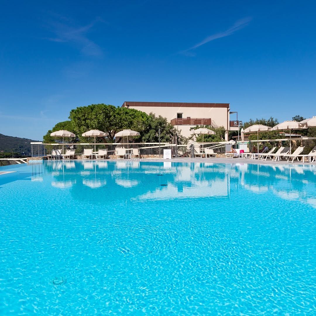 Ein klarer Pool spiegelt den blauen Himmel wider, umgeben von Liegen und Sonnenschirmen in einer ruhigen Umgebung.