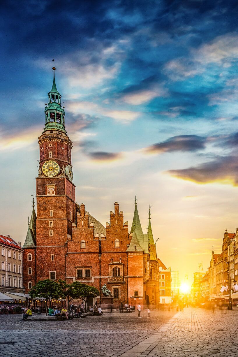 Die rote Backsteinkirche mit Türmen strahlt im Sonnenuntergang, umgeben von historischem Stadtflair und Menschen.