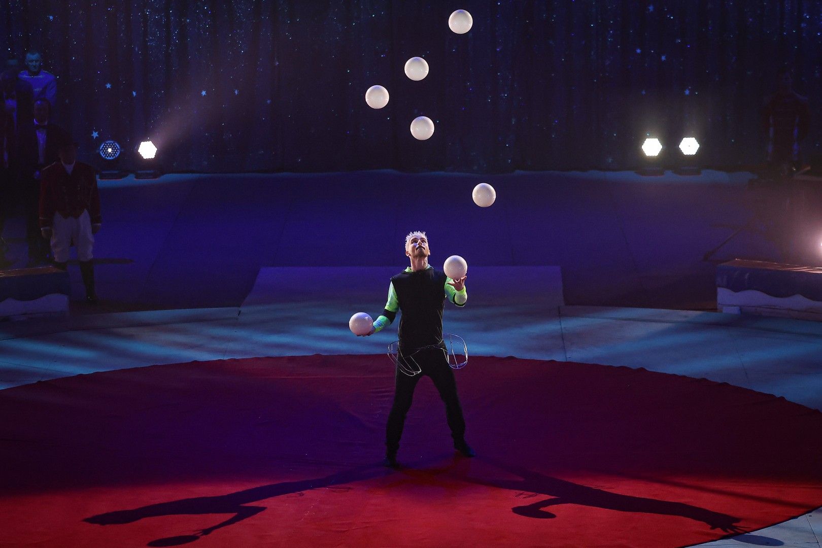 Ein Jongleur mit bunten Lichtern jongliert mehrere weiße Bälle in der Manege eines Zirkus.