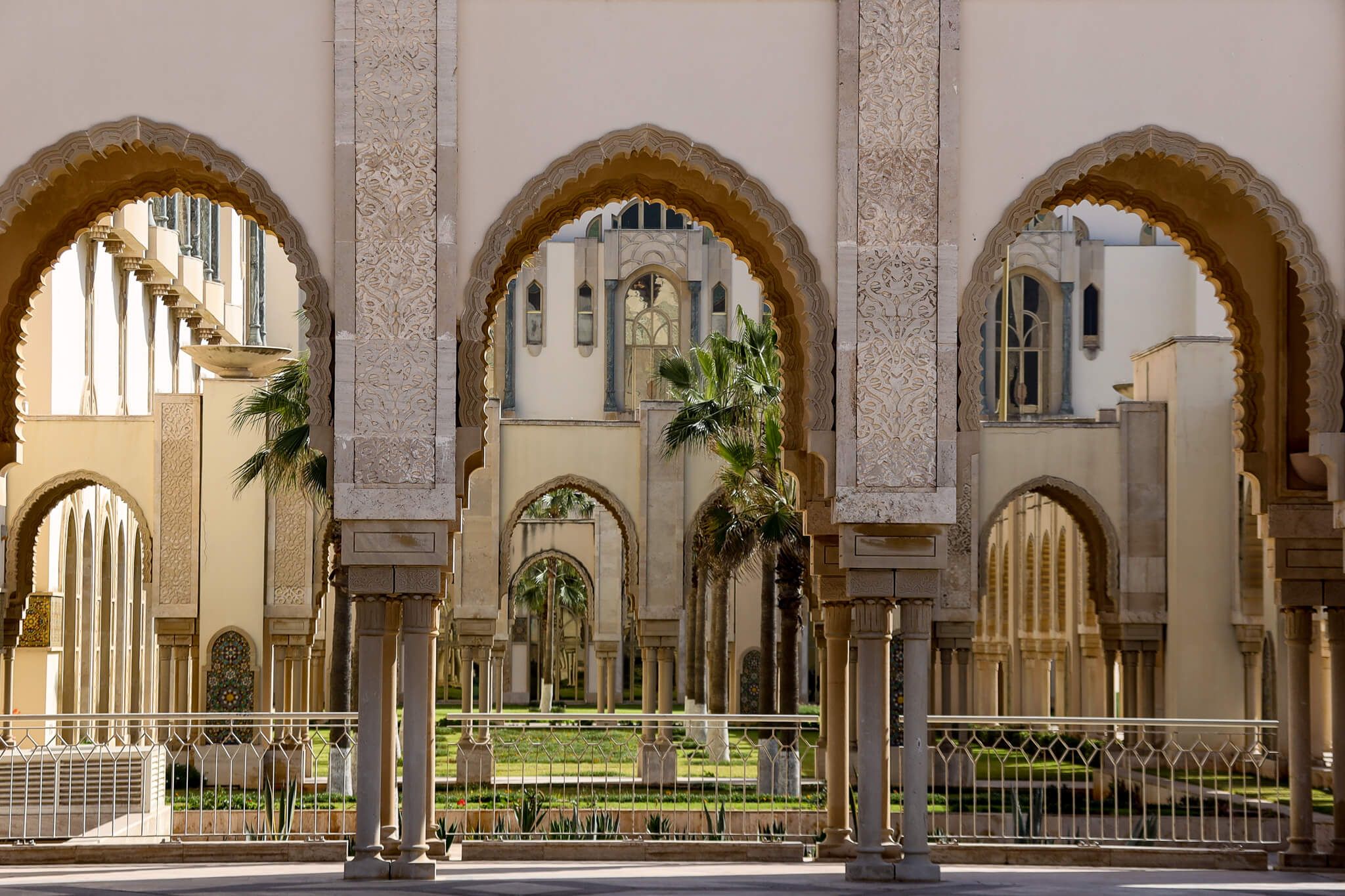 Ein architektonisches Bild mit kunstvollen Bögen, Palmen und einem schönen Garten im Hintergrund.