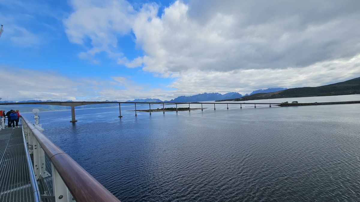 Eine malerische Aussicht auf eine Brücke über ruhiges Wasser, umgeben von Bergen und einem bewölkten Himmel.