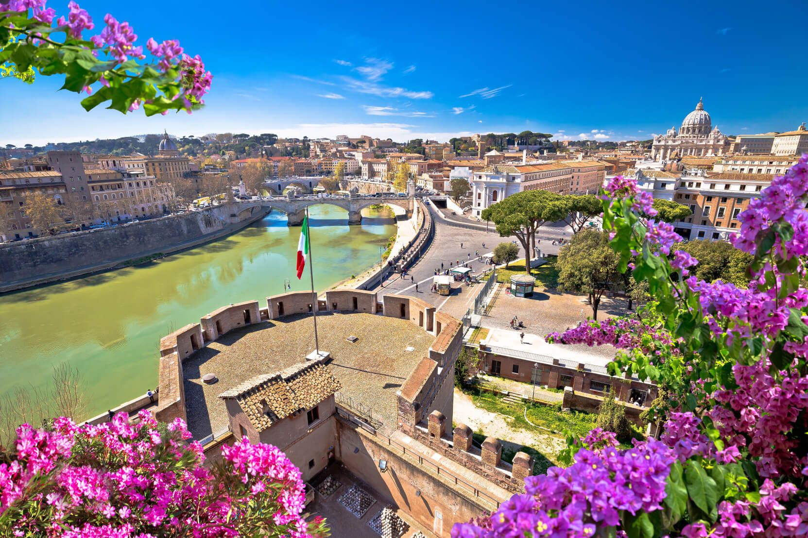 Blick auf Rom mit der Tiber, Brücken und bunten Blumen im Vordergrund. Ein schöner, sonniger Tag.