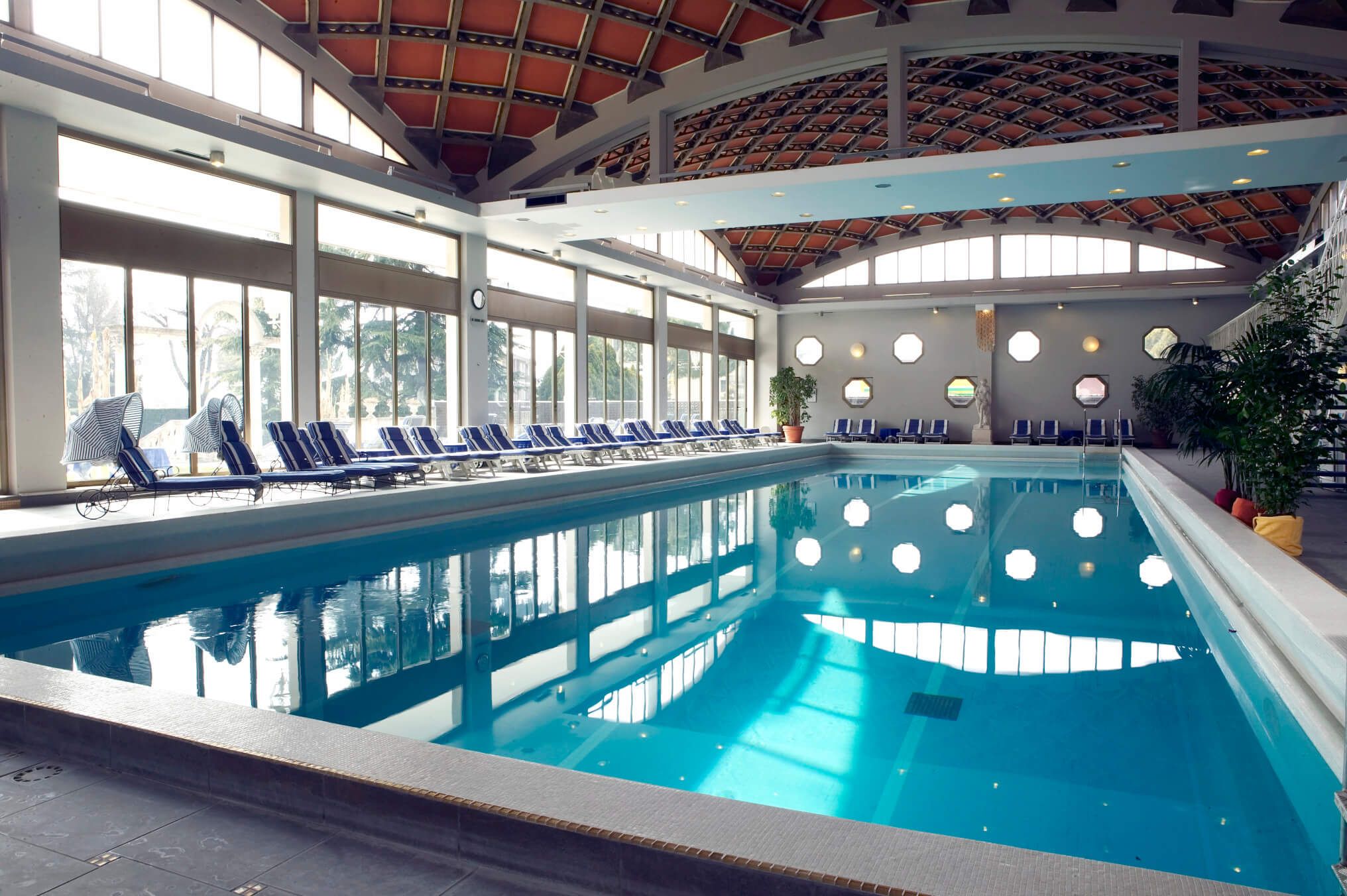 Ein eleganter Innenpool mit Liegen, großen Fenstern und einem beeindruckenden Dach. Ruhe und Entspannung pur.