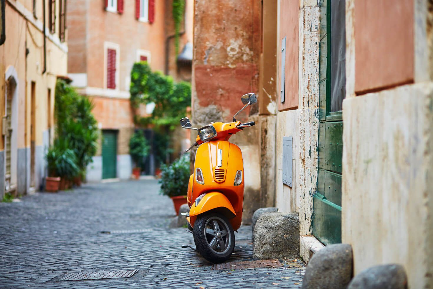 Eine orangefarbene Vespa steht an einer ruhigen, gepflasterten Gasse zwischen historischen Gebäuden.