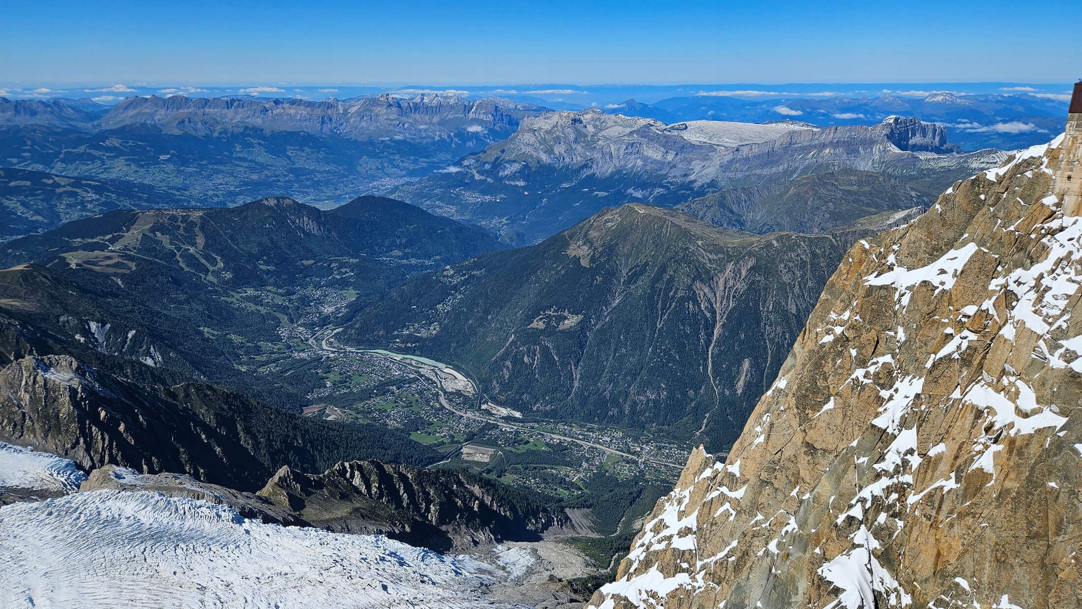 Atemberaubende Berglandschaft mit schneebedeckten Gipfeln und grünen Tälern unter einem klaren blauen Himmel.