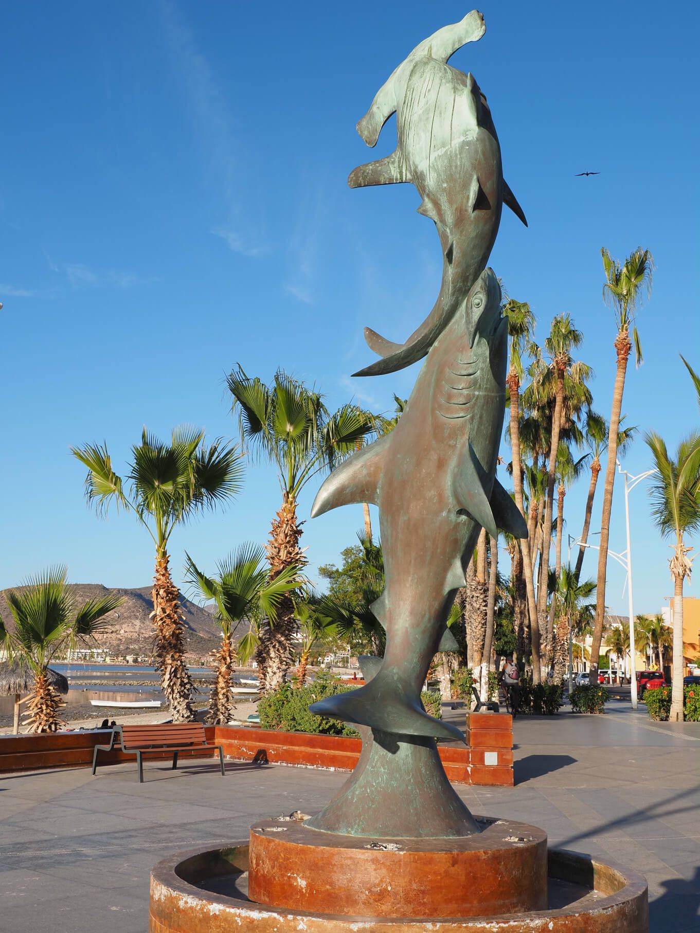Eine beeindruckende Statue von zwei Fischen vor Palmen und einem blauen Himmel am Meer.