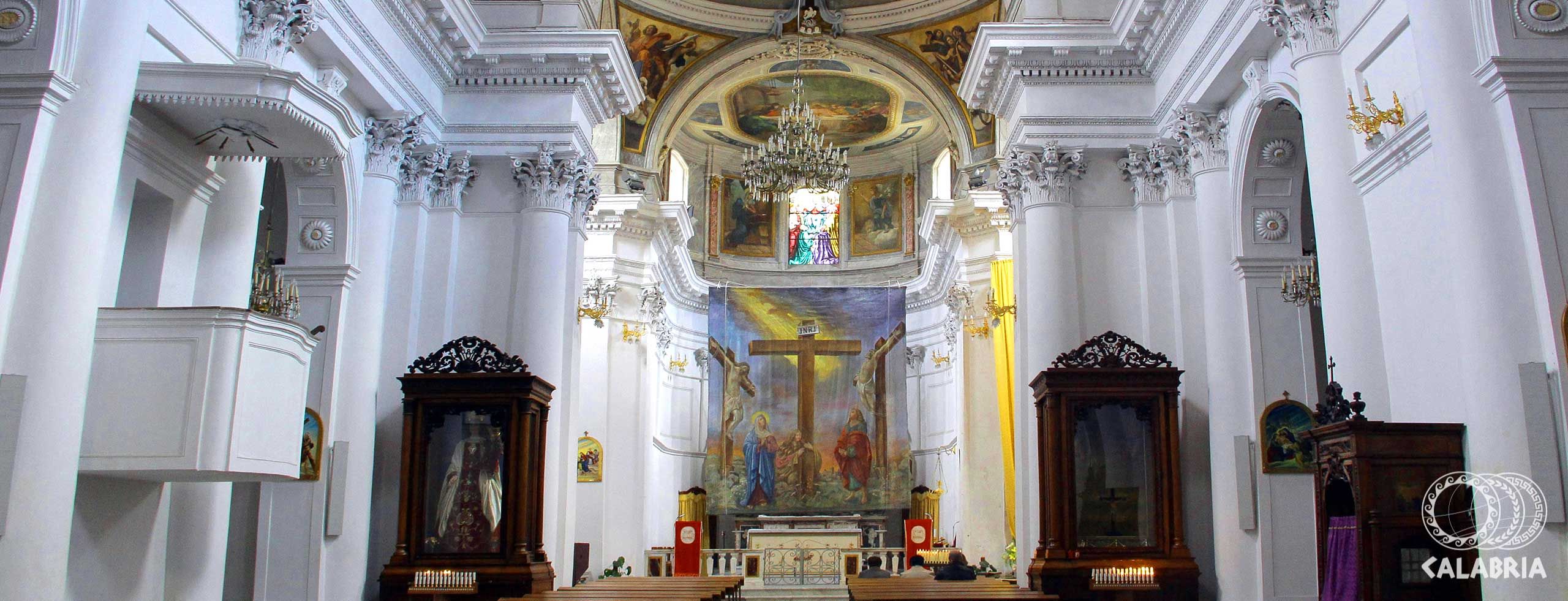 Imposante Kirche mit hohen weißen Wänden, Fresken, altächtigen Möbeln und einem zentralen Kreuz.