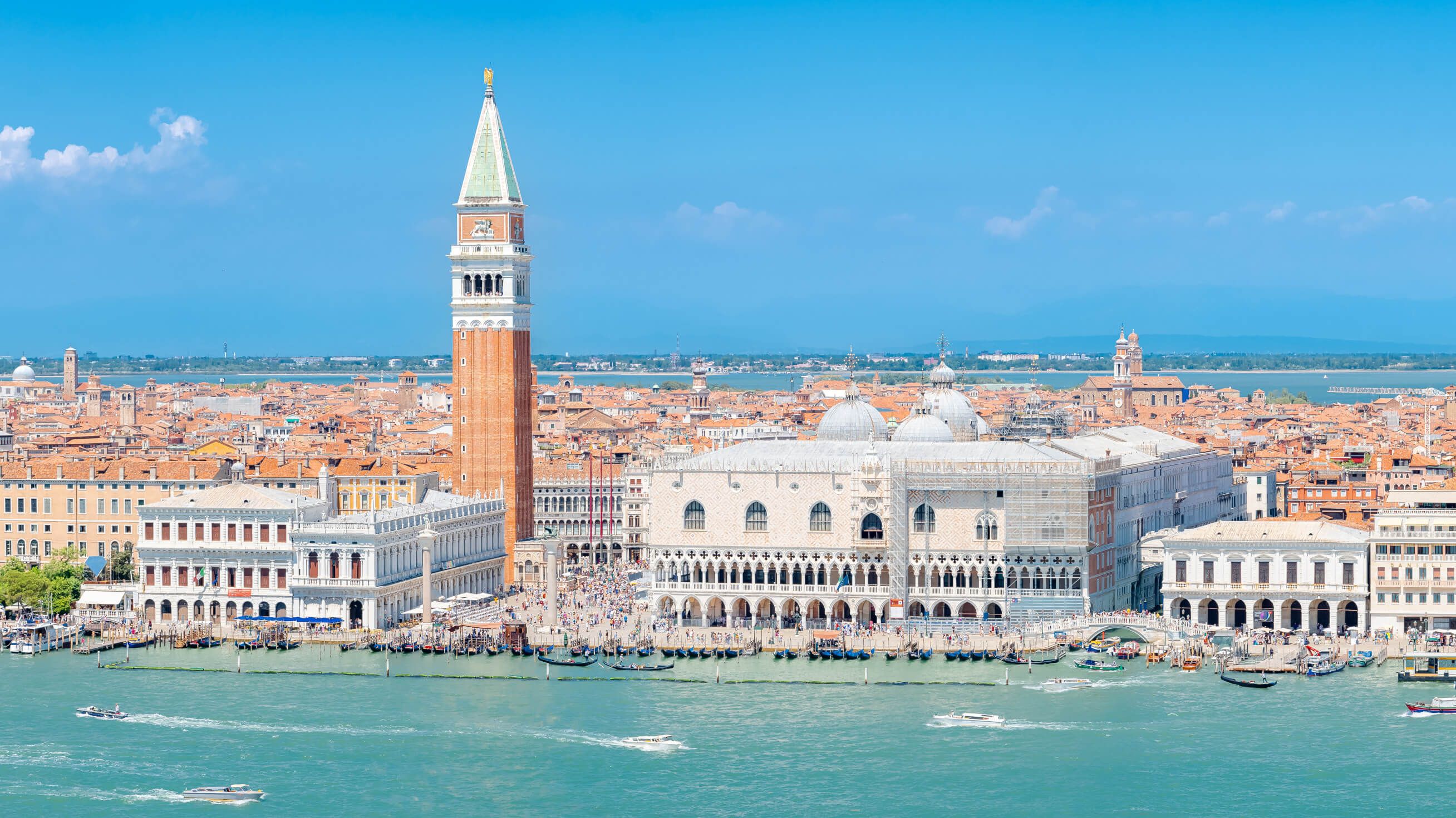 Der Markusplatz in Venedig, mit dem Campanile und dem Dogenpalast, umgeben von sanftem Wasser und blauen Himmel.