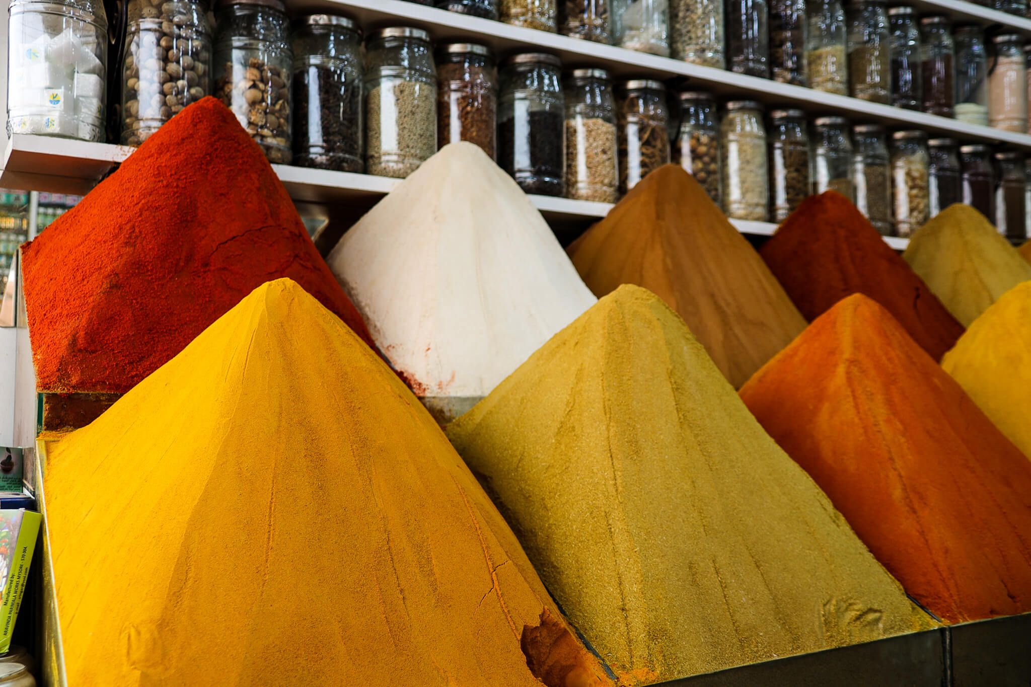 Bunte Gewürzhaufen in verschiedenen Formen und Farben, im Hintergrund Gläser mit verschiedenen Zutaten.