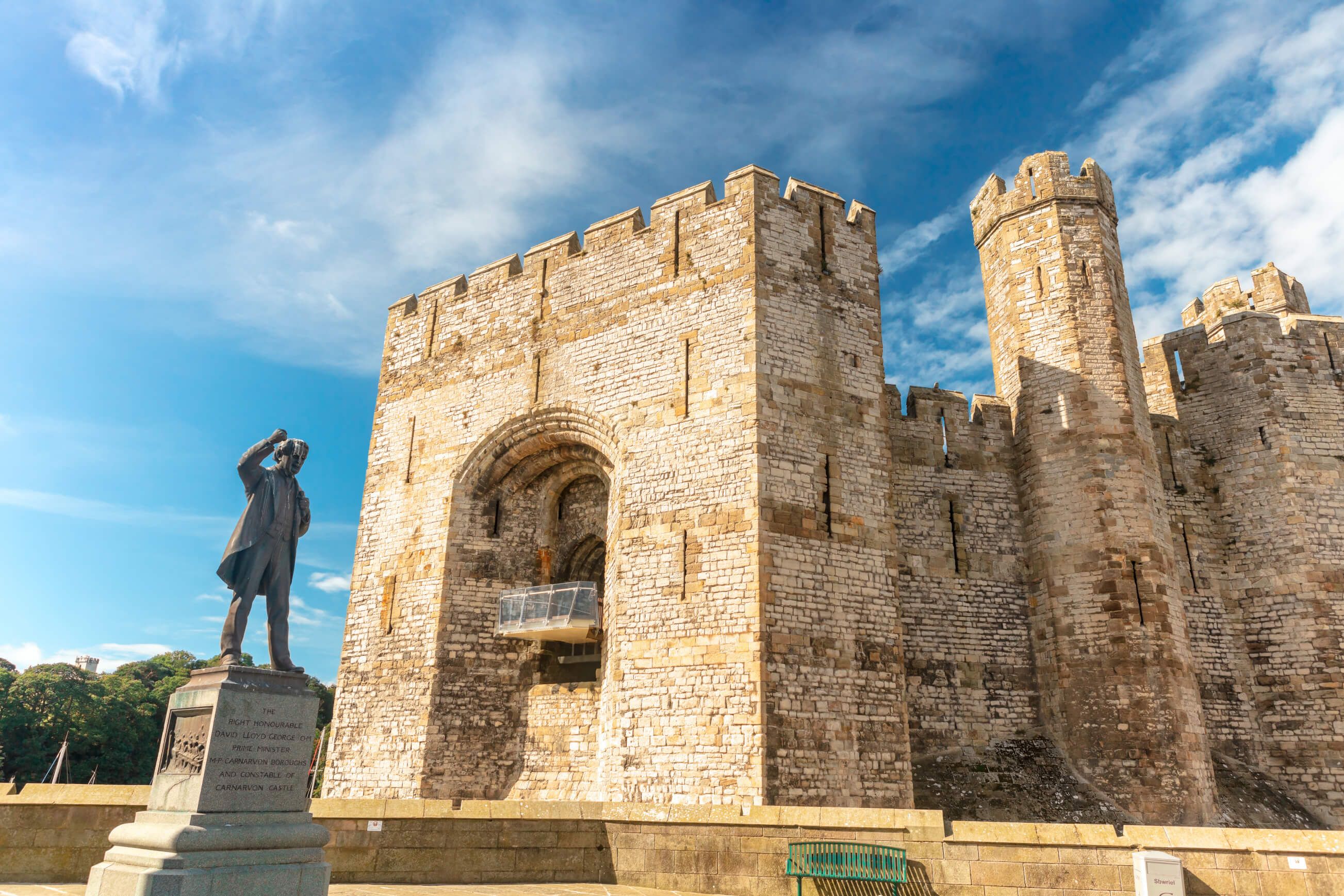 Ein historisches Schloss in Wales mit einer Statue im Vordergrund und blauem Himmel. Eindrucksvolle Architektur und Textur.