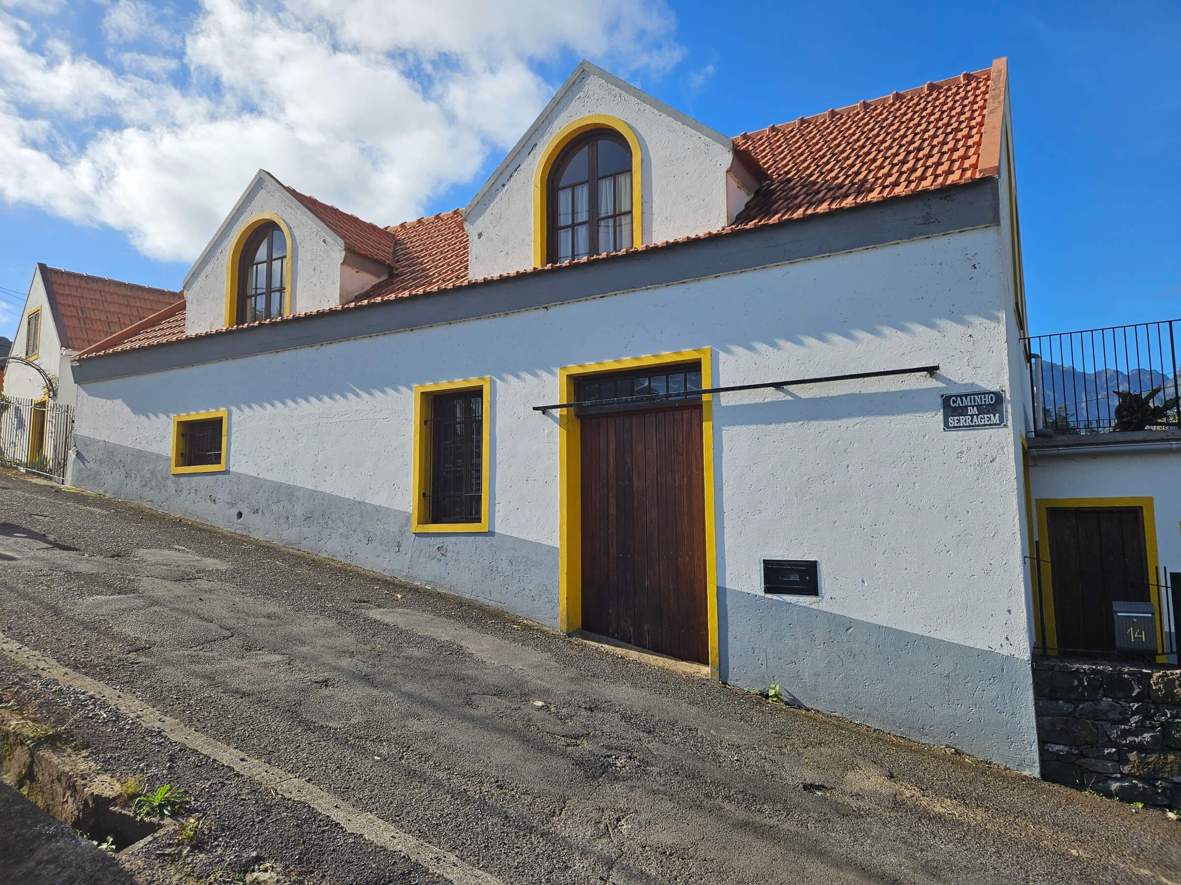 Eine weiße, zweigeschossige Gebäude mit gelben Akzenten, liegend an einer steilen Straße unter blauen Himmel.