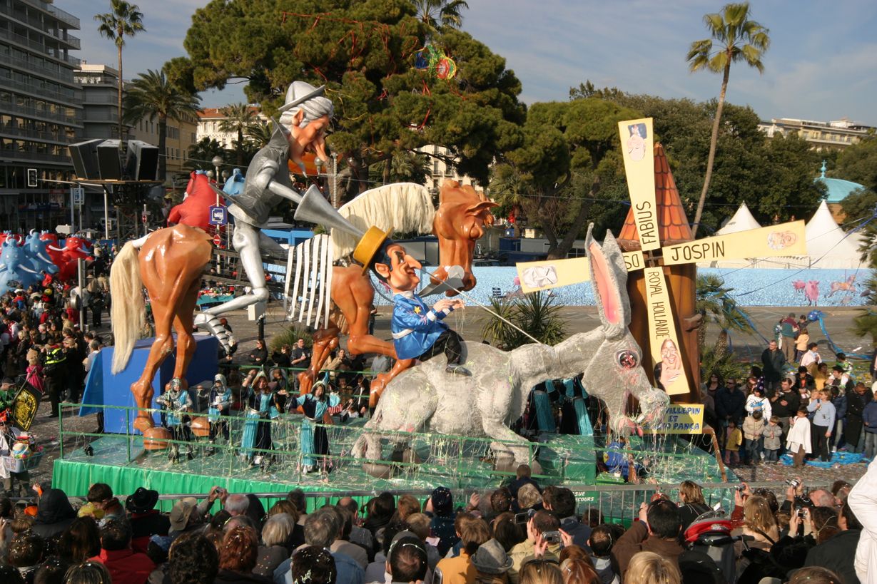 Umzugswagen mit bunten Figuren und einem großen Hasen, viele Zuschauer in Feierlaune, sonniger Tag.