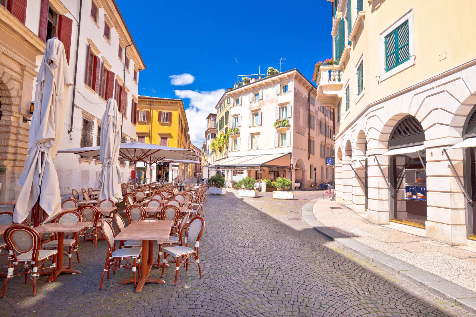 Gemütliche Straße mit Cafés und Tischen, umgeben von bunten Gebäuden und blauem Himmel.