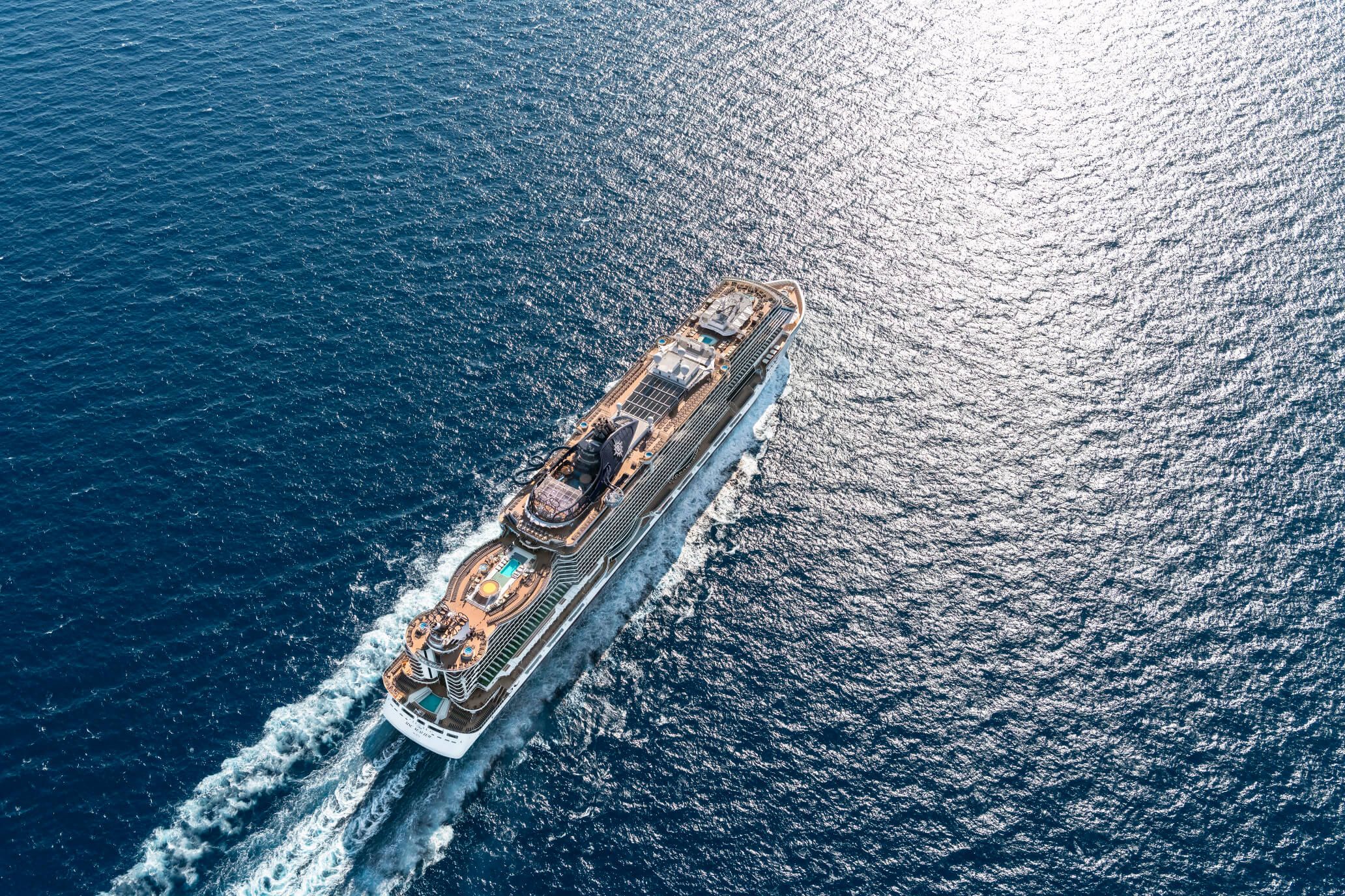 Ein großes Kreuzfahrtschiff fährt über das blaue Wasser, die Sonne spiegelt sich auf der Oberfläche.