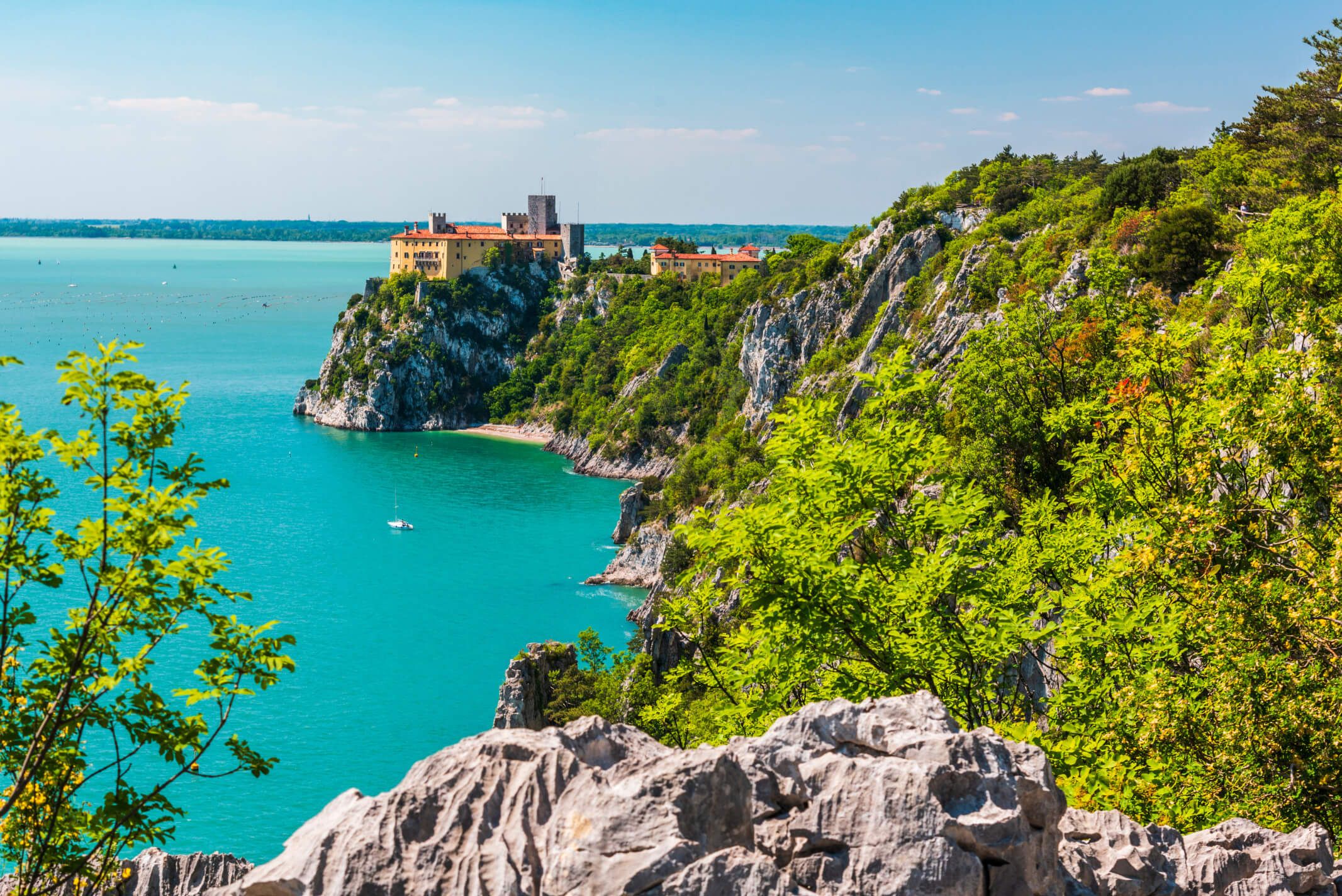 Eine malerische Küstenansicht mit klarem blauen Wasser, Felsen und einer historischen Festung im Hintergrund.