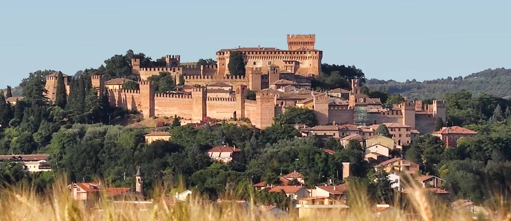 Eine beeindruckende Burg thront über einer Landschaft, umgeben von Bäumen und kleinen Häusern.