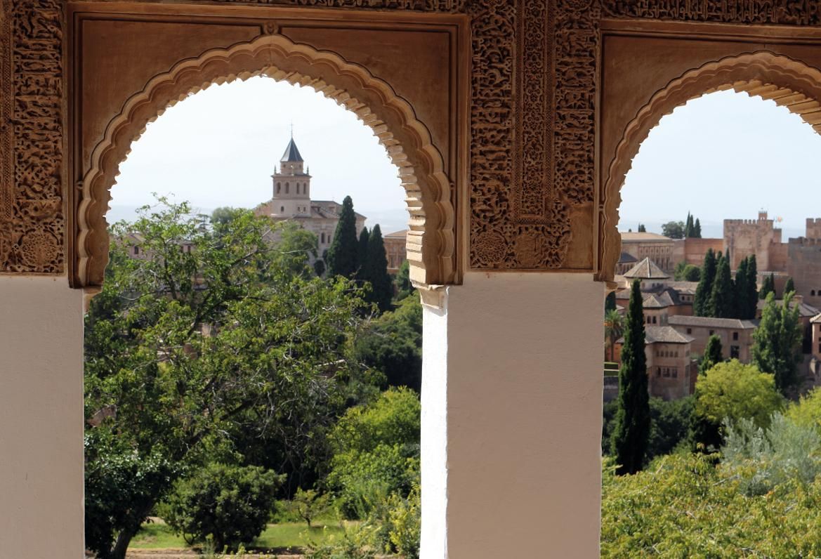 Blick durch kunstvolle Bögen auf die Alhambra und die umgebende grüne Landschaft. Historische Schönheit vereint.