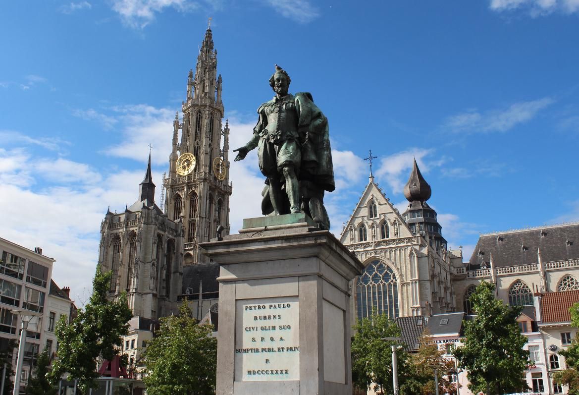 Statuen von Peter Paul Rubens vor beeindruckender Architektur und blauem Himmel in einer Stadtansicht.