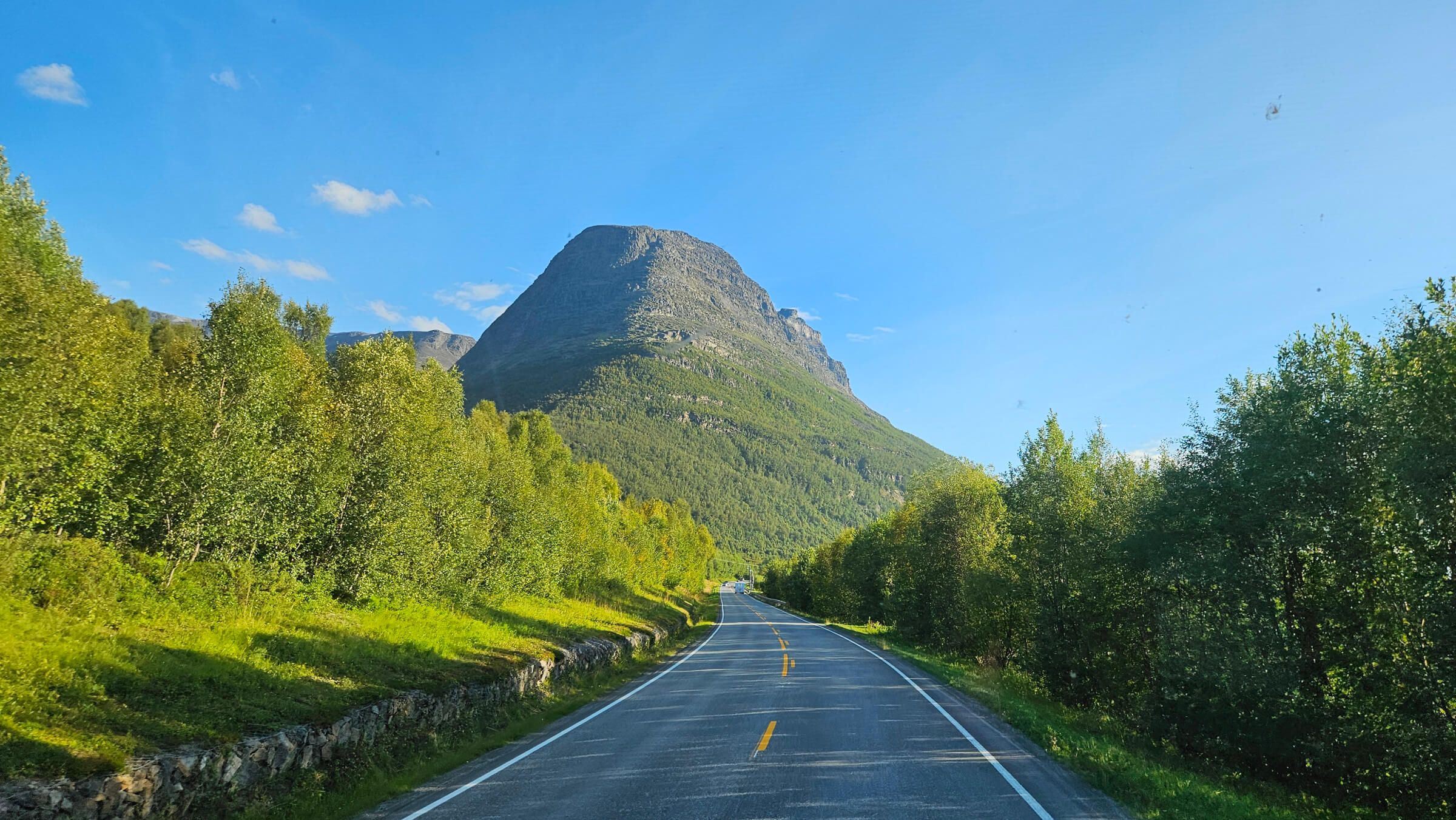 Eine kurvenreiche Straße umgeben von Bäumen und einem beeindruckenden Berg unter blauem Himmel.