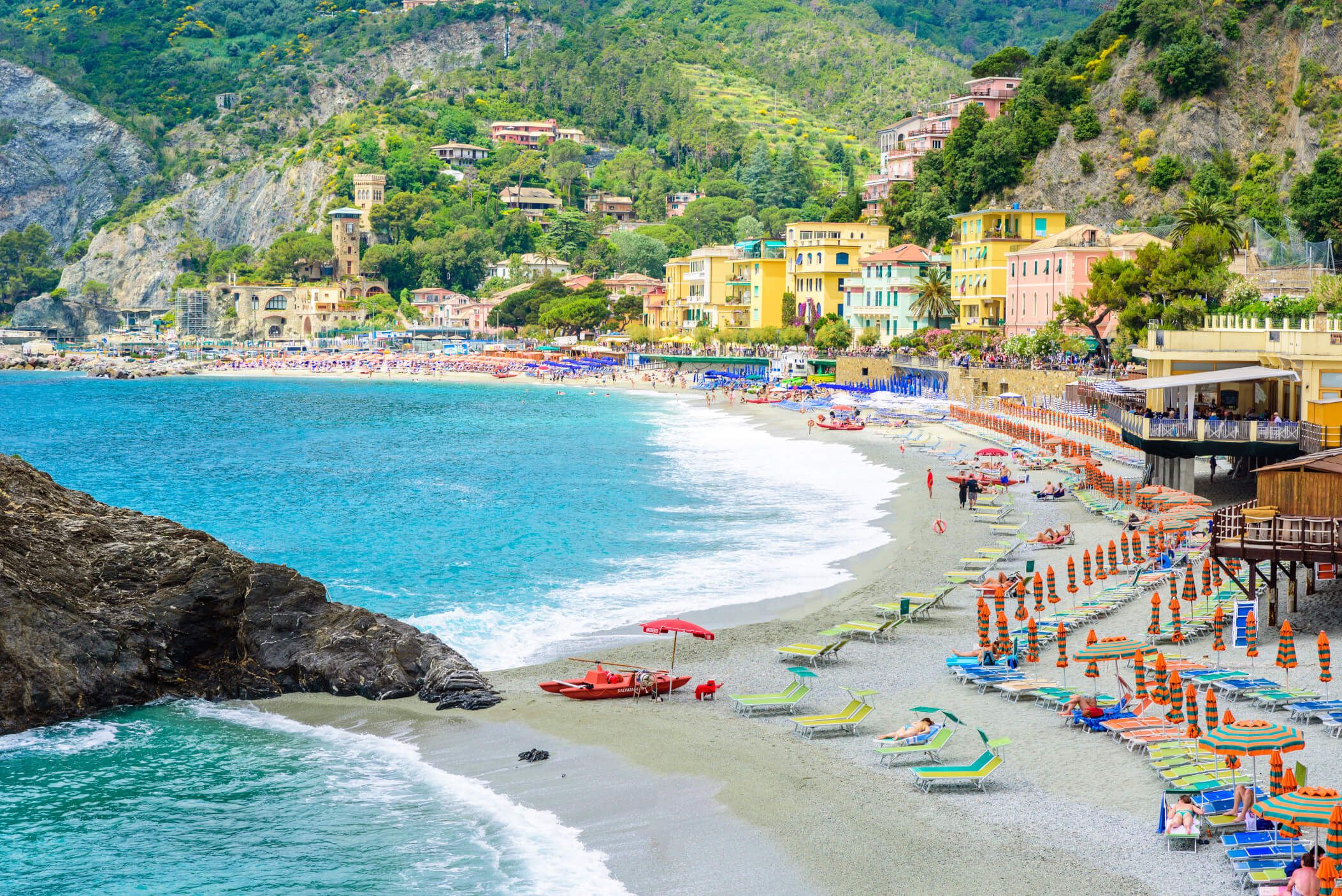 Schöner Strand mit vielen Liegen und bunten Sonnenschirmen, umgeben von bunten Häusern und Bergen.
