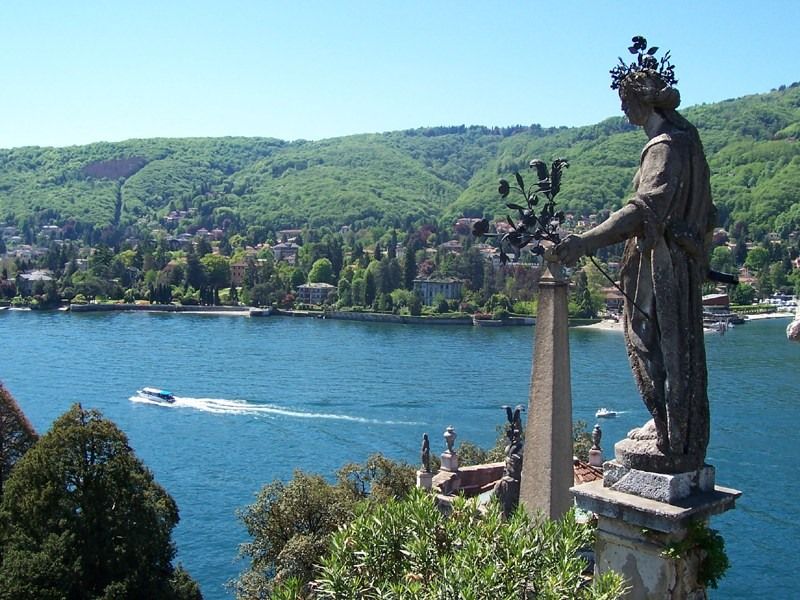 Eine Statue blickt auf einen malerischen See, umgeben von grünen Hügeln und schönen Villen.