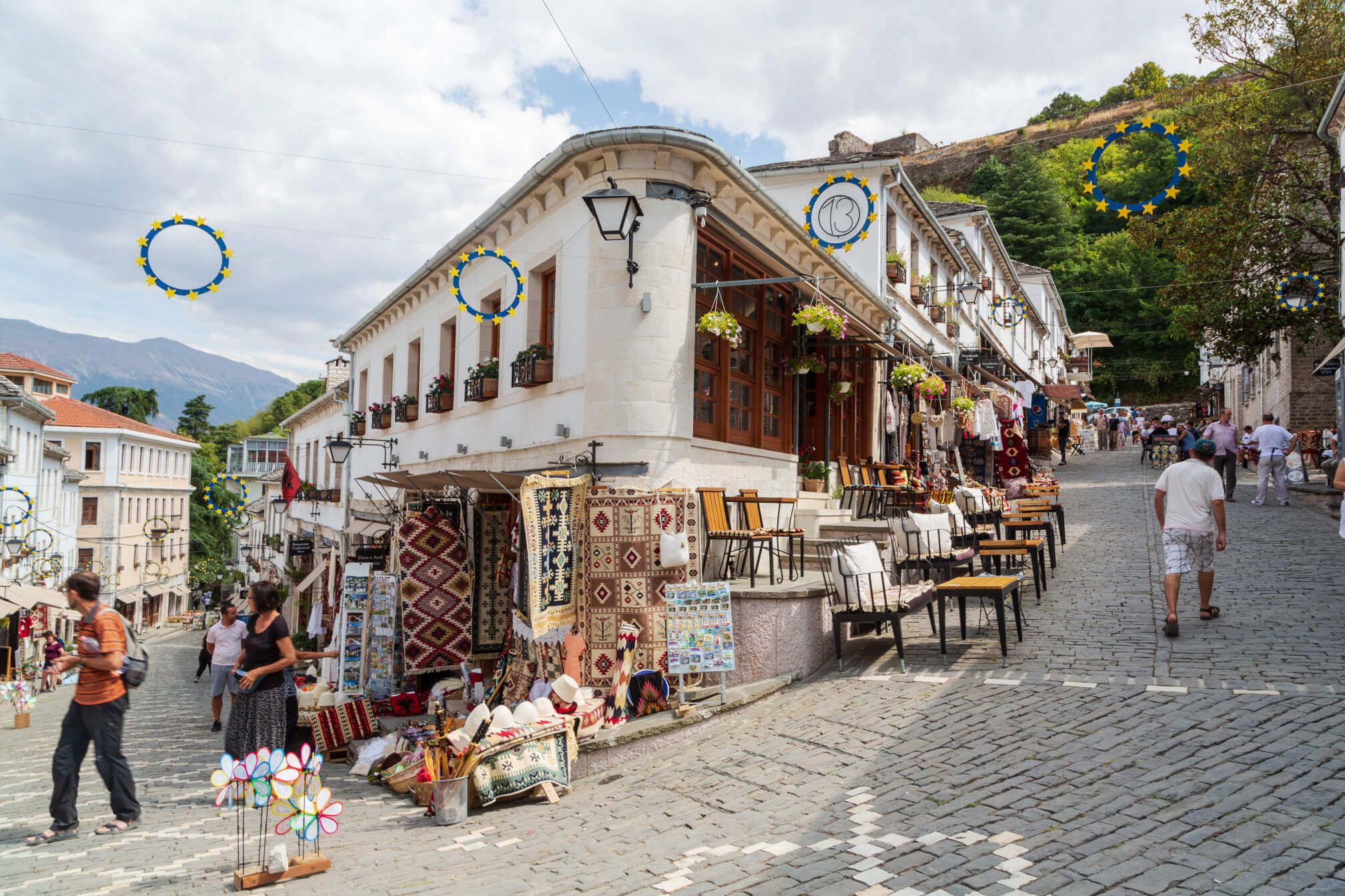 Eine belebte Straße mit Geschäften, Cafés und bunten Teppichen in einer malerischen Stadt.