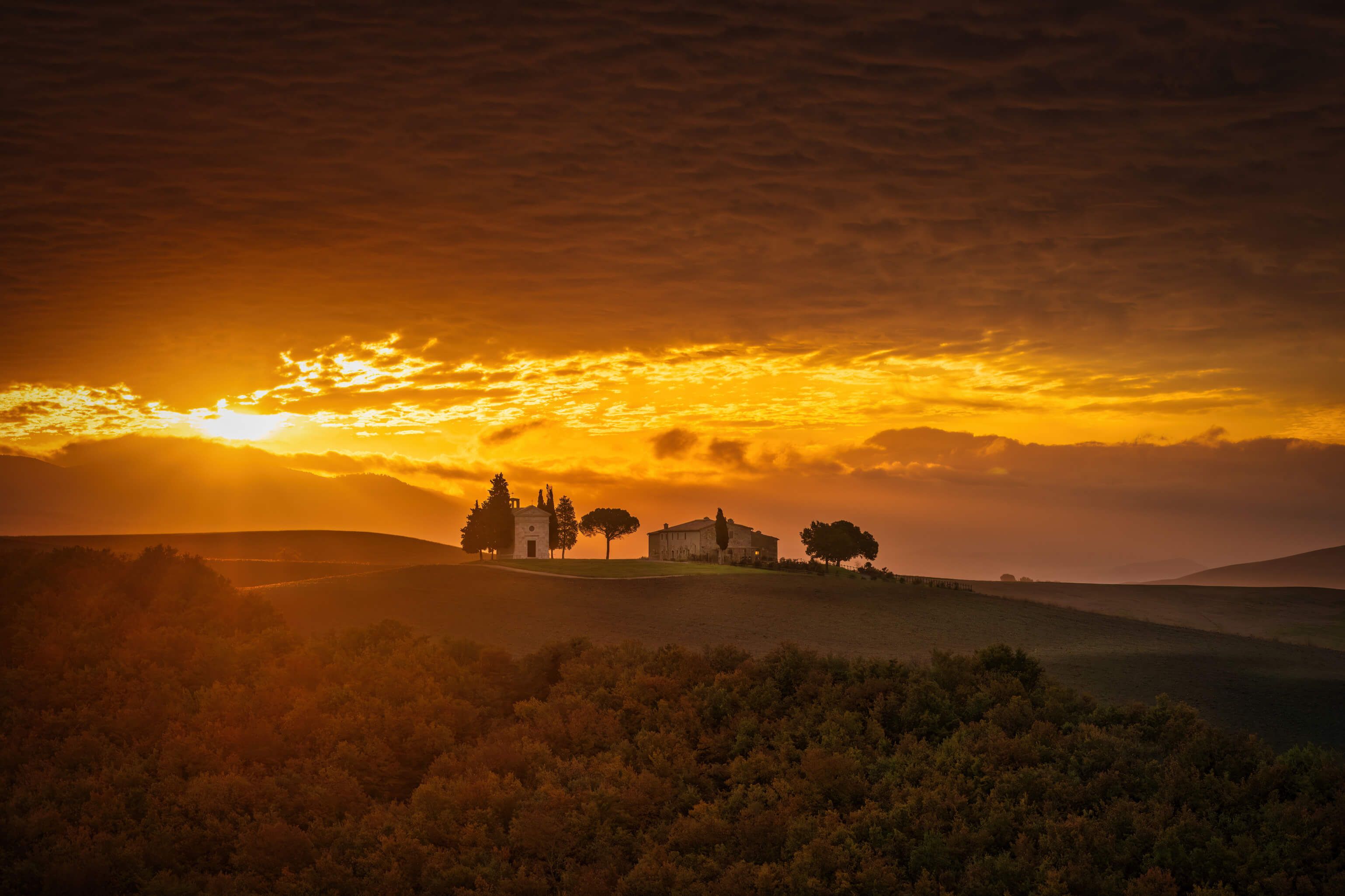 Eine malerische Landschaft bei Sonnenuntergang mit Hügeln, Bäumen und geheimnisvollen Gebäuden.