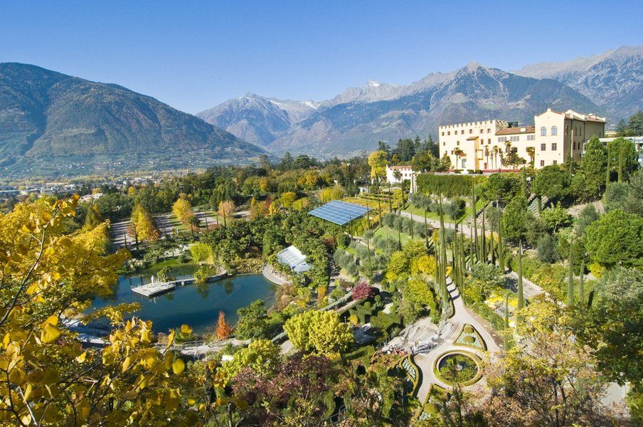 Schöne Landschaft mit einem Schloss, bunten Gärten und Bergen im Hintergrund, klarer blauer Himmel.