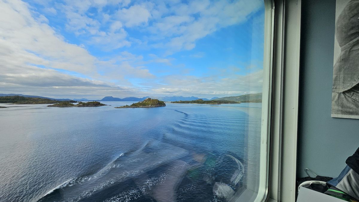 Ein Blick aus dem Fenster auf einen ruhigen Wasserweg, umgeben von Inseln und blauem Himmel mit Wolken.