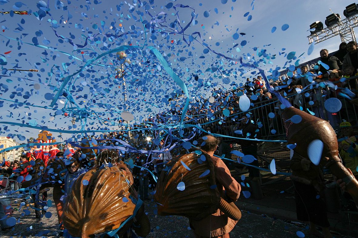 Bunte Konfetti-Explosion während eines Festumzugs, fröhliche Menschen feiern unter blauem Himmel.