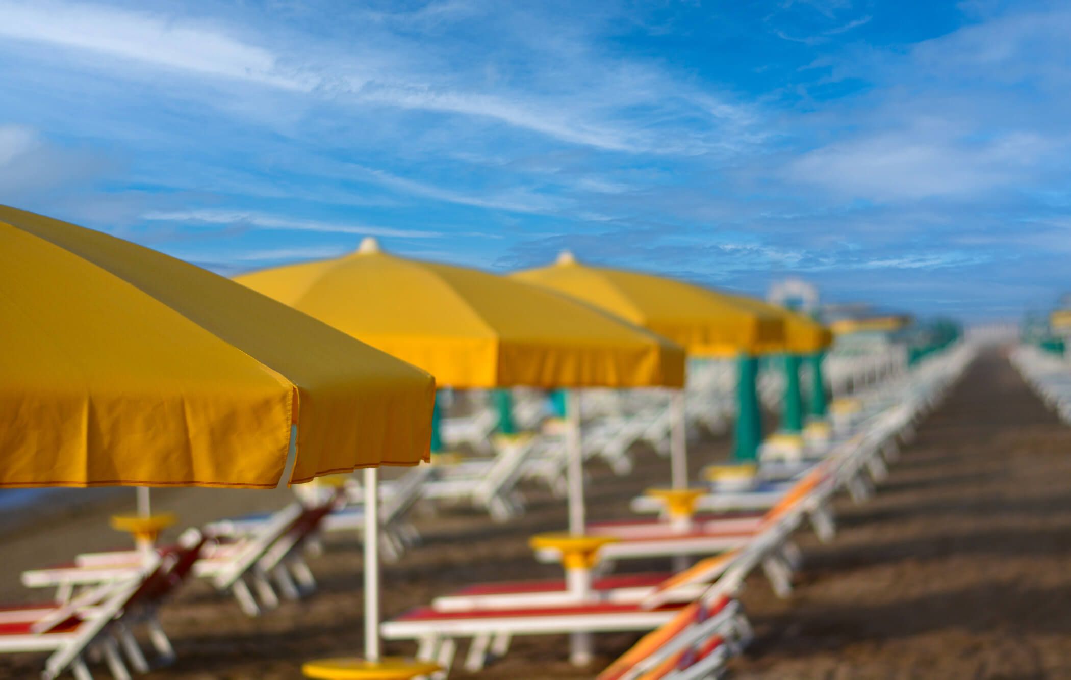 Ein Strand mit gelben Sonnenschirmen und Liegen, die in der Ferne verschwommen sind, unter einem blauen Himmel.