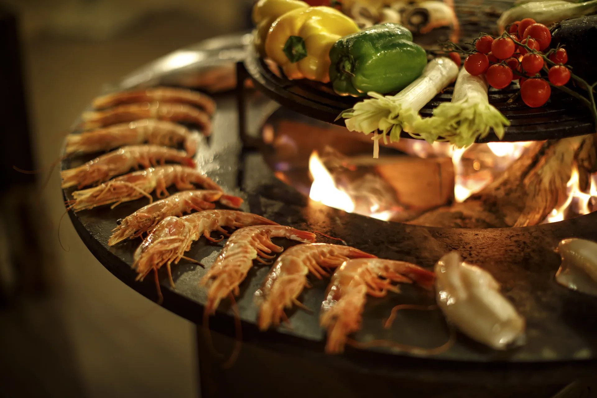 Frische Garnelen und Gemüse liegen auf einem Grill über offenem Feuer, das eine gemütliche Atmosphäre schafft.