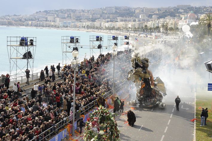 Eine große Menschenmenge schaut beim Karneval in Nizza einem Drachenumzug am Strand zu. Festliche Stimmung überall!
