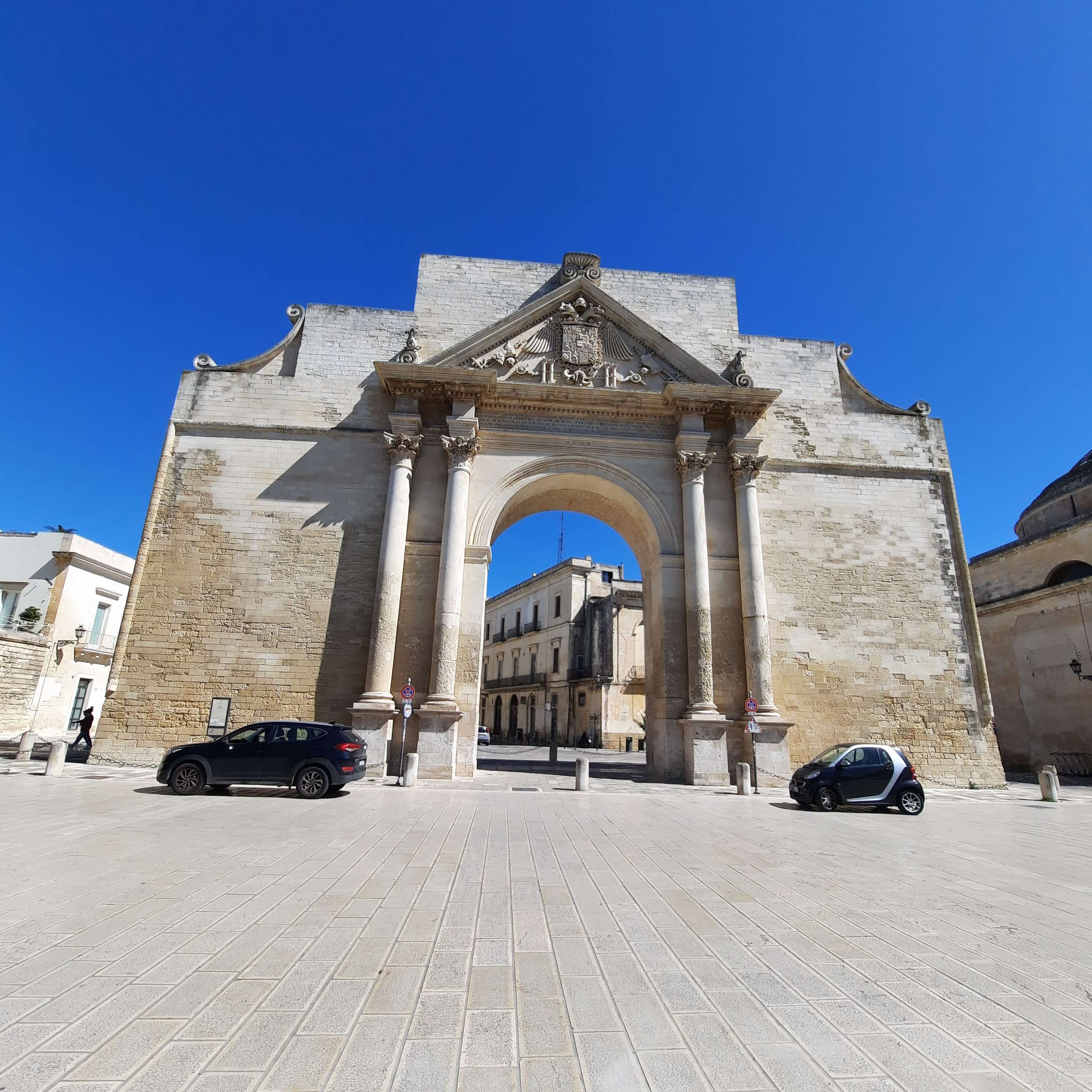Ein beeindruckendes Tor mit Säulen, umgeben von historischen Gebäuden und blauem Himmel.