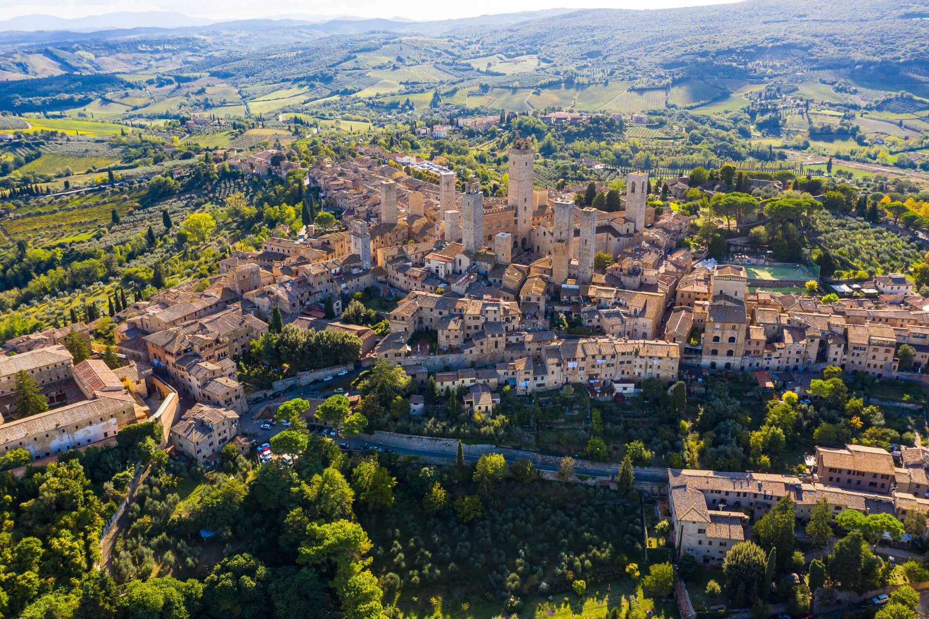 Eine malerische Stadt mit Türmen, umgeben von grünen Hügeln und Weinbergen in der Toskana.
