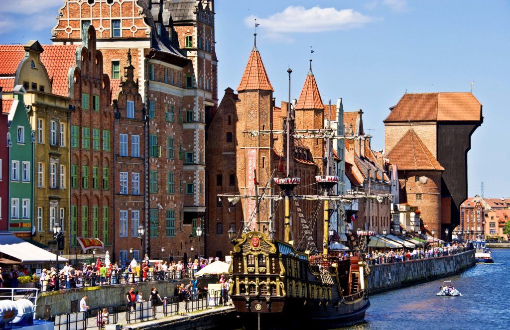 Historische Gebäude am Fluss mit einem Schiff, viele Menschen und blauer Himmel. Ein lebendiger, schöner Ort.