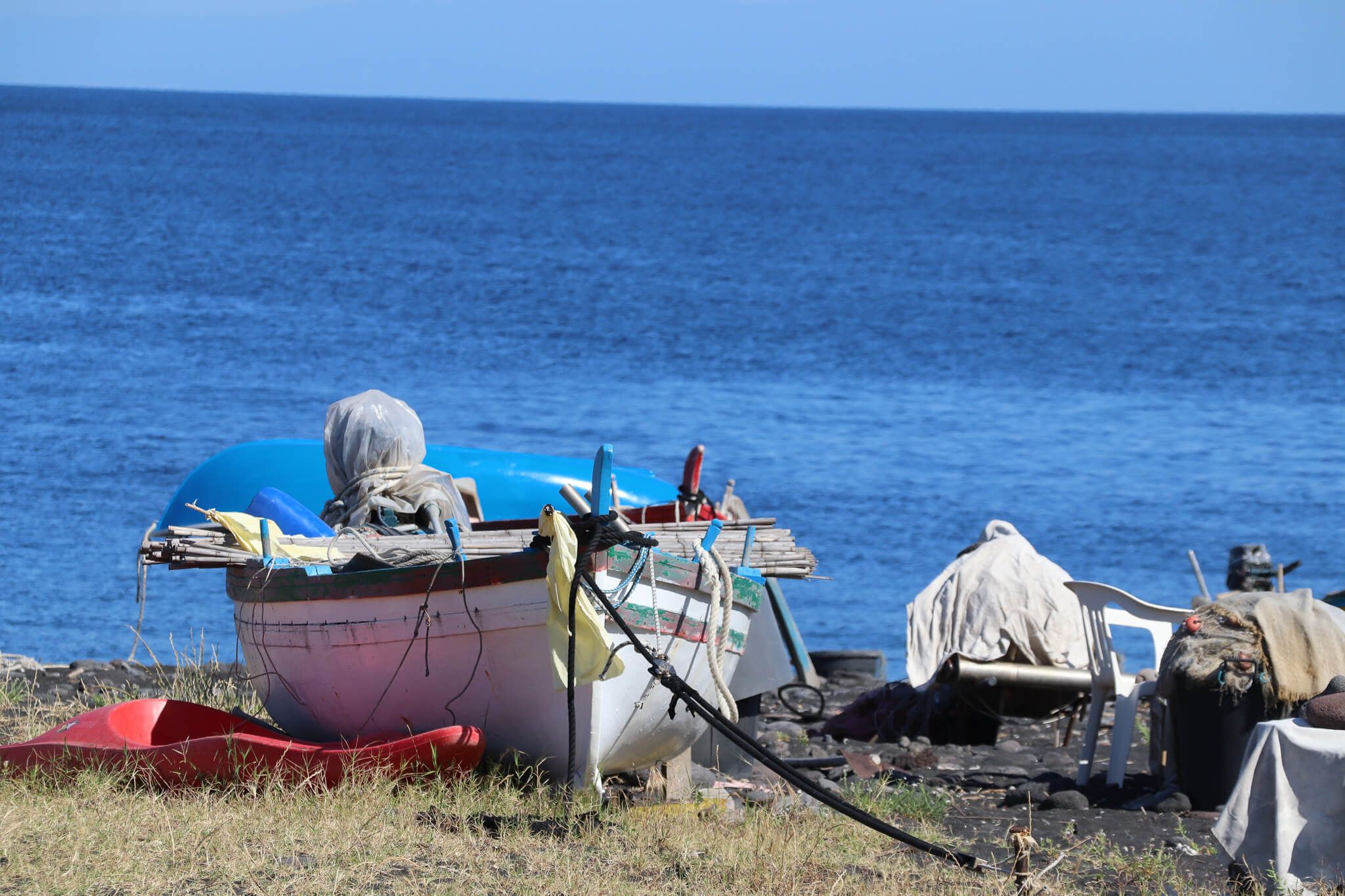 Ein Boot steht am Strand, umgeben von einem ruhigen blauen Meer und einigen verstreuten Gegenständen.